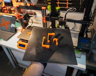 Orange 3D prints on a build plate in the workshop