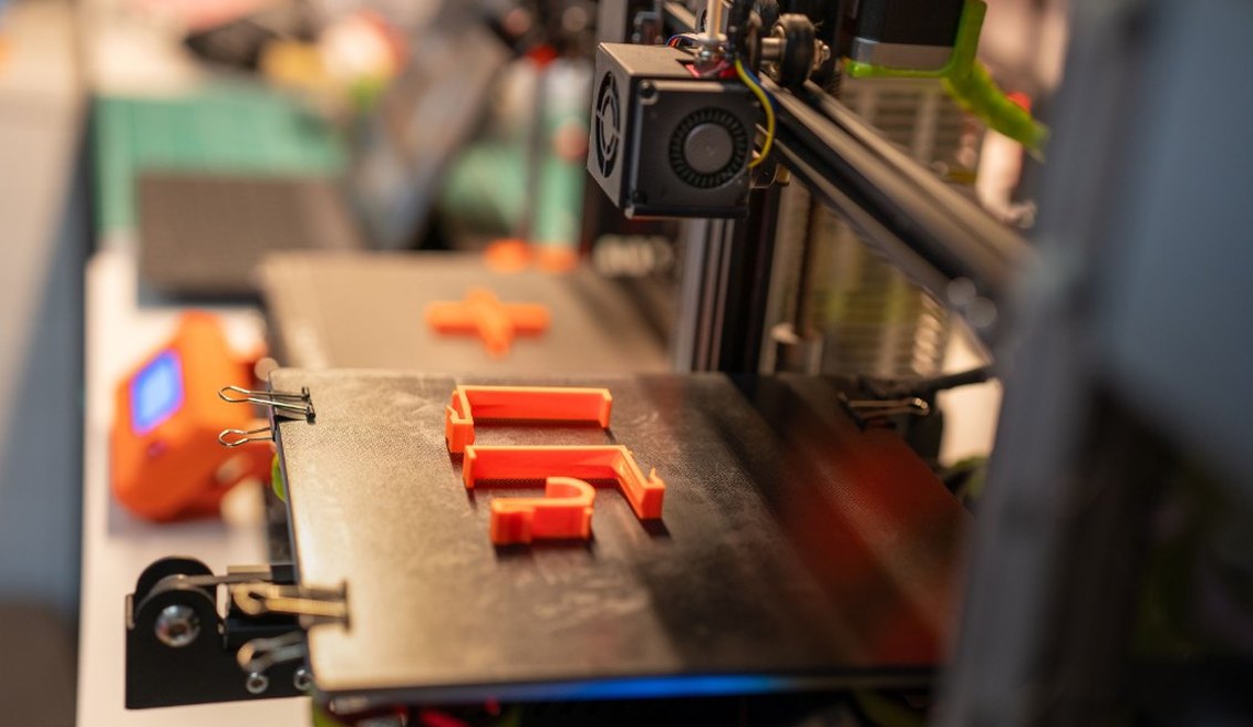 3D printer laying down orange parts on the build plate